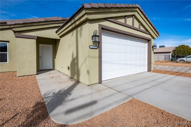 exterior space featuring a garage, concrete driveway, a tile roof, and stucco siding