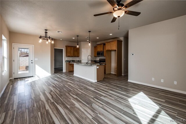 kitchen featuring dark wood finished floors, appliances with stainless steel finishes, open floor plan, hanging light fixtures, and a kitchen island with sink