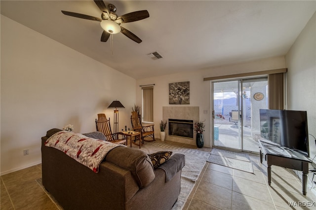 tiled living room featuring ceiling fan, a tile fireplace, visible vents, baseboards, and vaulted ceiling