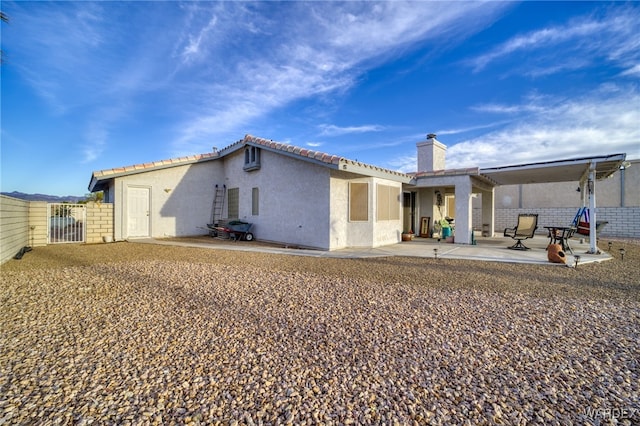 back of property with a chimney, a patio area, a tile roof, and stucco siding