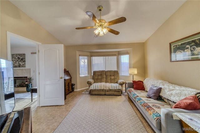 living room featuring baseboards, a tiled fireplace, ceiling fan, vaulted ceiling, and light tile patterned flooring