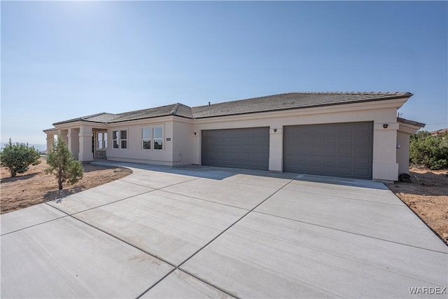 prairie-style home with a garage, a tile roof, driveway, and stucco siding