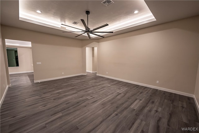 spare room with a ceiling fan, a raised ceiling, visible vents, and dark wood-style flooring