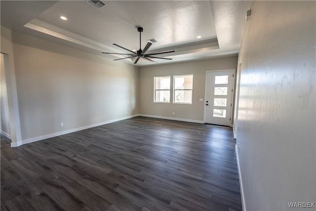 spare room with dark wood-style flooring, visible vents, a ceiling fan, baseboards, and a tray ceiling