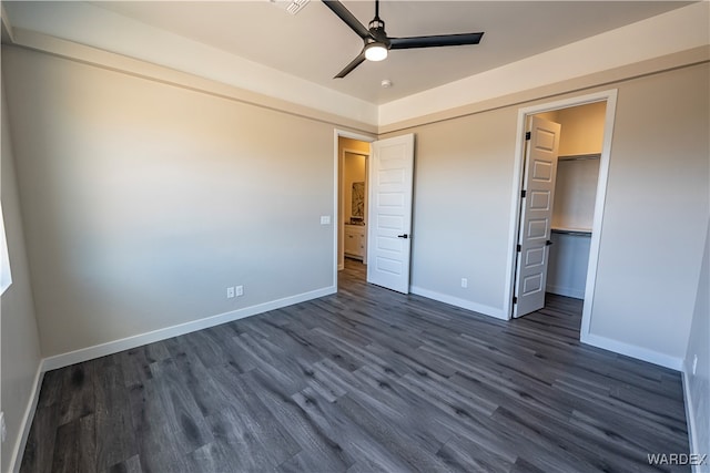 unfurnished bedroom with a walk in closet, baseboards, dark wood finished floors, and a closet