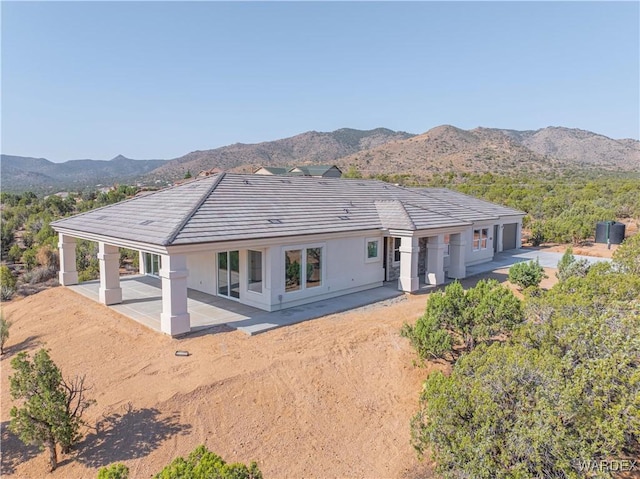 rear view of house with stucco siding, a patio, dirt driveway, and a mountain view