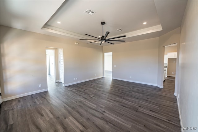 unfurnished room featuring baseboards, visible vents, a tray ceiling, and dark wood-type flooring