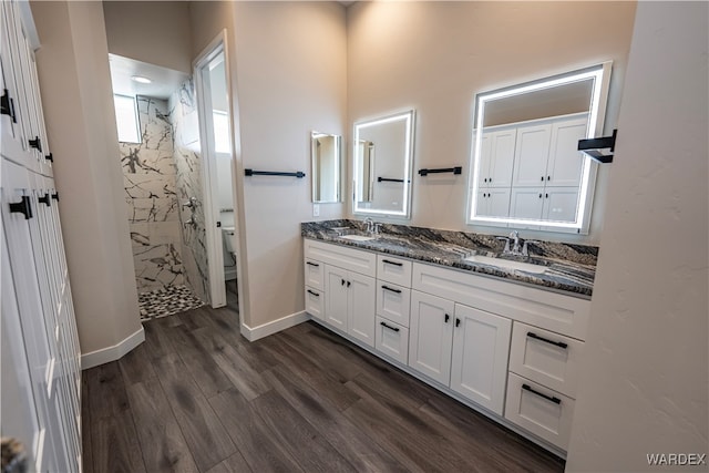 bathroom with double vanity, a sink, a marble finish shower, and wood finished floors