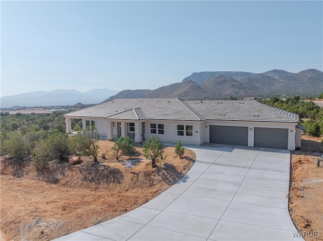 ranch-style home with an attached garage, a mountain view, concrete driveway, and stucco siding