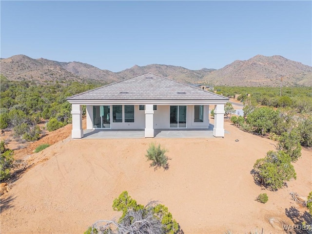 back of house with stucco siding, a mountain view, and a patio