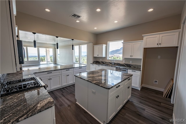 kitchen featuring dark stone counters, a kitchen island, white cabinetry, and pendant lighting