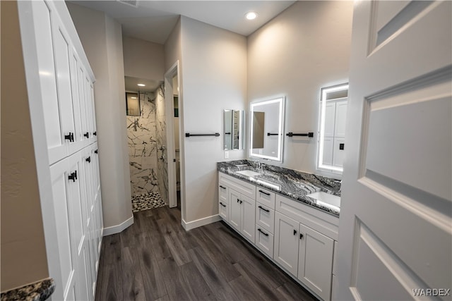 bathroom featuring a sink, double vanity, a walk in shower, and wood finished floors