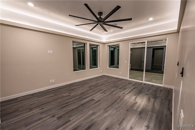 spare room featuring a tray ceiling, dark wood-style flooring, recessed lighting, ceiling fan, and baseboards