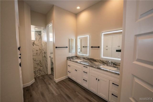 full bathroom featuring double vanity, wood finished floors, a sink, and a marble finish shower