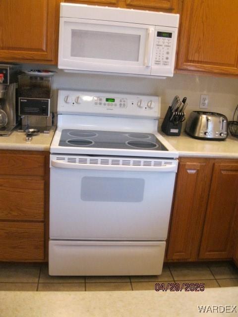 kitchen with brown cabinetry, light countertops, light tile patterned floors, and white appliances