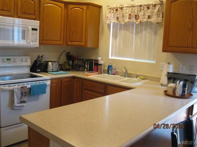 kitchen with a sink, light countertops, brown cabinets, and white appliances