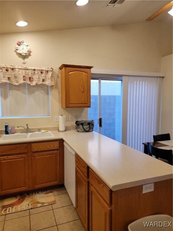 kitchen with a peninsula, white dishwasher, light countertops, a sink, and light tile patterned floors