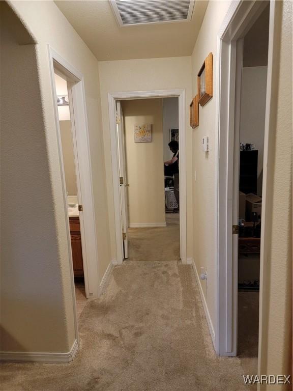 hall featuring visible vents, baseboards, and light carpet