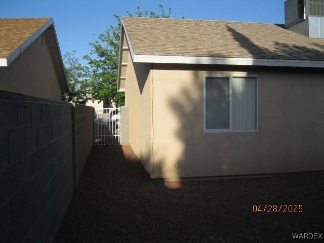 view of side of home featuring fence, a gate, roof with shingles, and stucco siding