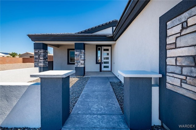 view of exterior entry featuring fence and stucco siding