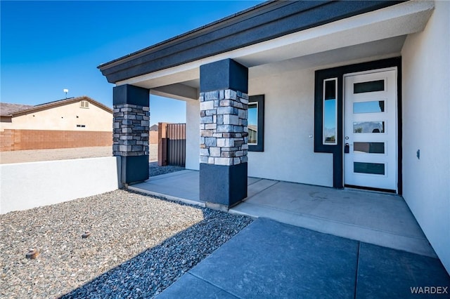 doorway to property with stone siding, fence, and stucco siding