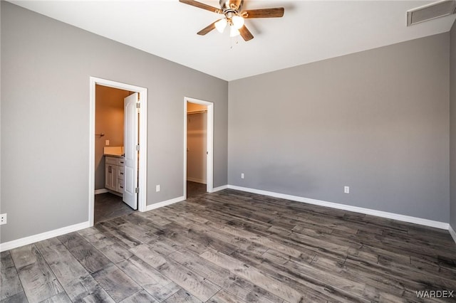 unfurnished bedroom with baseboards, visible vents, connected bathroom, dark wood-type flooring, and a spacious closet