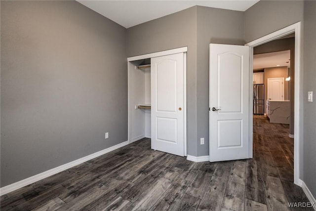 unfurnished bedroom with a closet, baseboards, dark wood-style flooring, and freestanding refrigerator