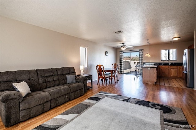 living room featuring a ceiling fan, visible vents, a textured ceiling, and wood finished floors