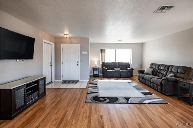 living room featuring baseboards, light wood-style flooring, visible vents, and a textured ceiling