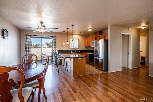 kitchen featuring dark countertops, freestanding refrigerator, a kitchen island, light wood-type flooring, and a kitchen breakfast bar