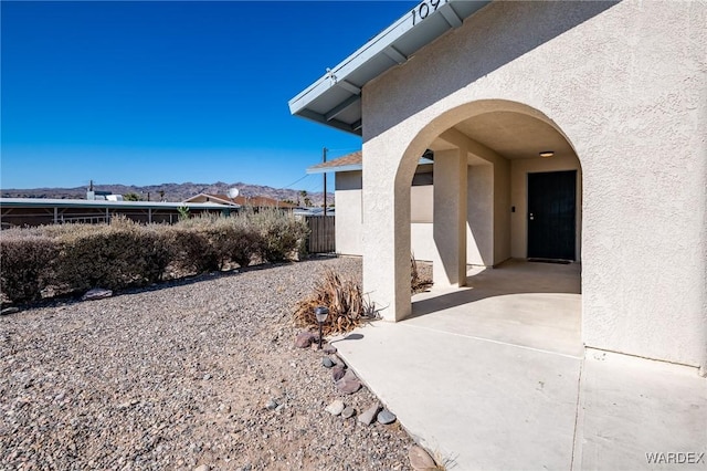 view of exterior entry featuring a mountain view, a patio, fence, and stucco siding