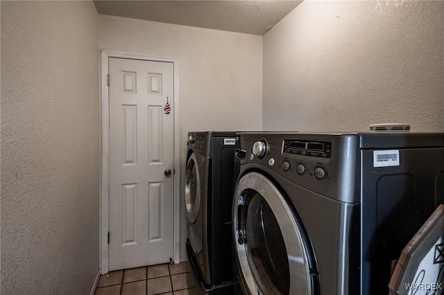 washroom with a textured wall, laundry area, separate washer and dryer, and light tile patterned flooring