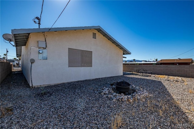 view of side of home with fence, a fire pit, and stucco siding