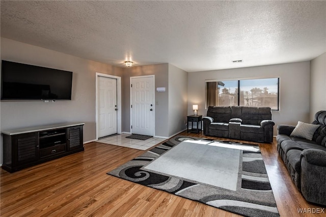 living area featuring visible vents, a textured ceiling, baseboards, and wood finished floors