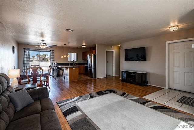 living area with visible vents, baseboards, a ceiling fan, light wood-style flooring, and a textured ceiling