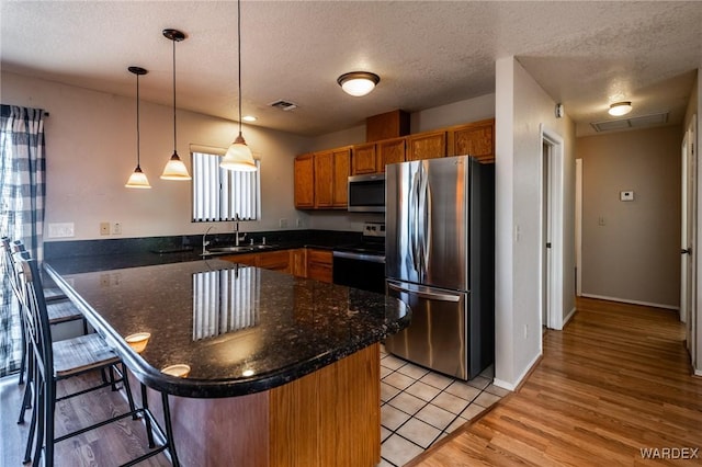 kitchen with stainless steel appliances, a peninsula, a sink, visible vents, and hanging light fixtures