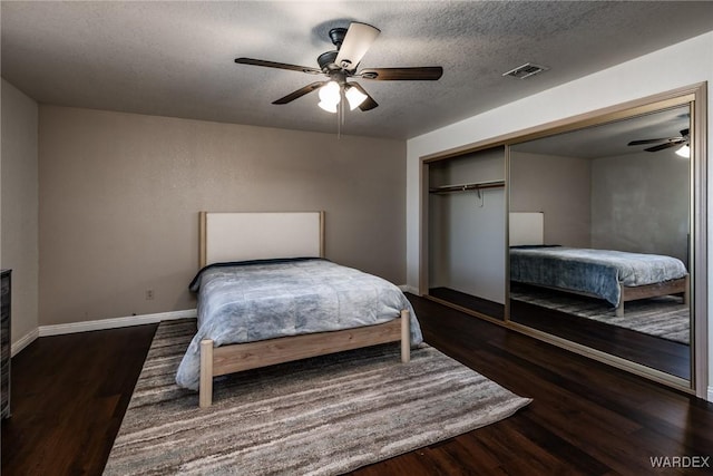 bedroom with baseboards, visible vents, dark wood finished floors, a textured ceiling, and a closet