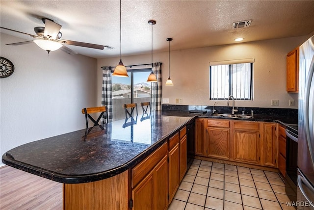 kitchen featuring a peninsula, a sink, visible vents, stainless steel electric range, and brown cabinets