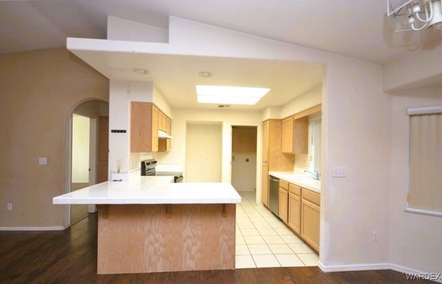 kitchen featuring arched walkways, stainless steel appliances, light brown cabinetry, a peninsula, and baseboards