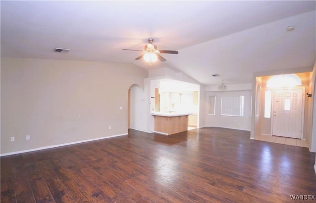 unfurnished living room with arched walkways, dark wood finished floors, visible vents, a ceiling fan, and vaulted ceiling