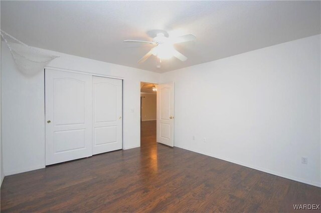 unfurnished bedroom featuring dark wood-type flooring, a closet, and a ceiling fan