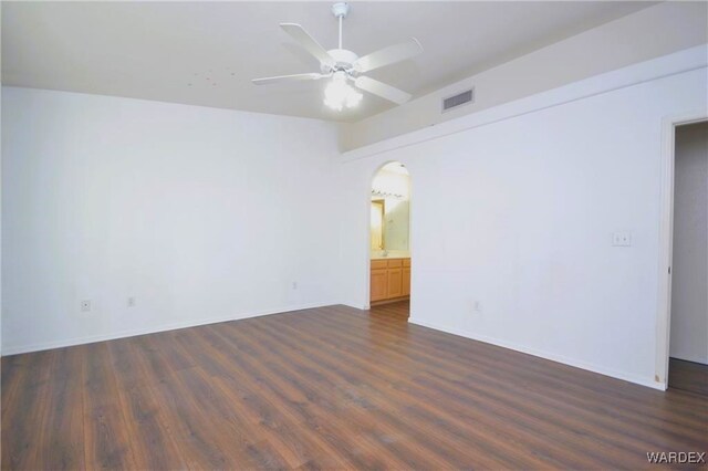 empty room with arched walkways, visible vents, dark wood finished floors, and a ceiling fan