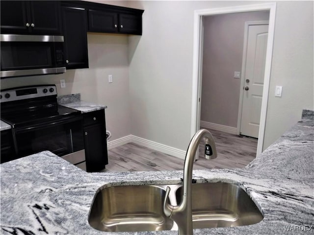 kitchen with light wood finished floors, stainless steel appliances, a sink, light stone countertops, and dark cabinetry