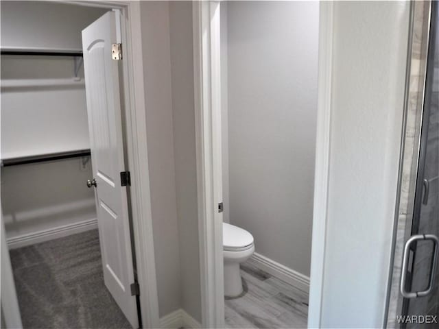 bathroom featuring baseboards, toilet, wood finished floors, a walk in closet, and a shower stall