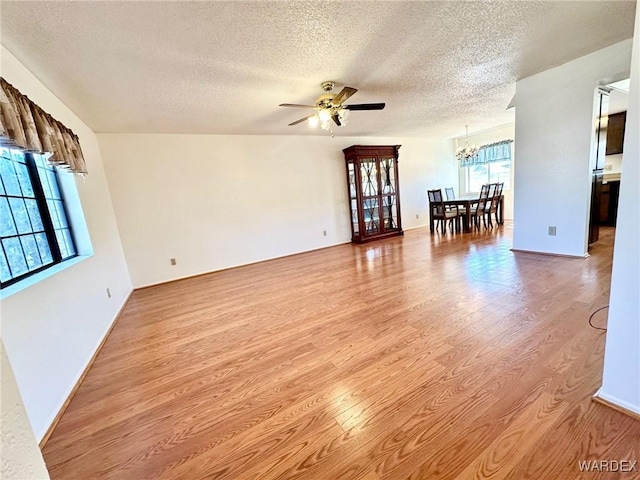 spare room with ceiling fan with notable chandelier, a textured ceiling, and light wood-type flooring