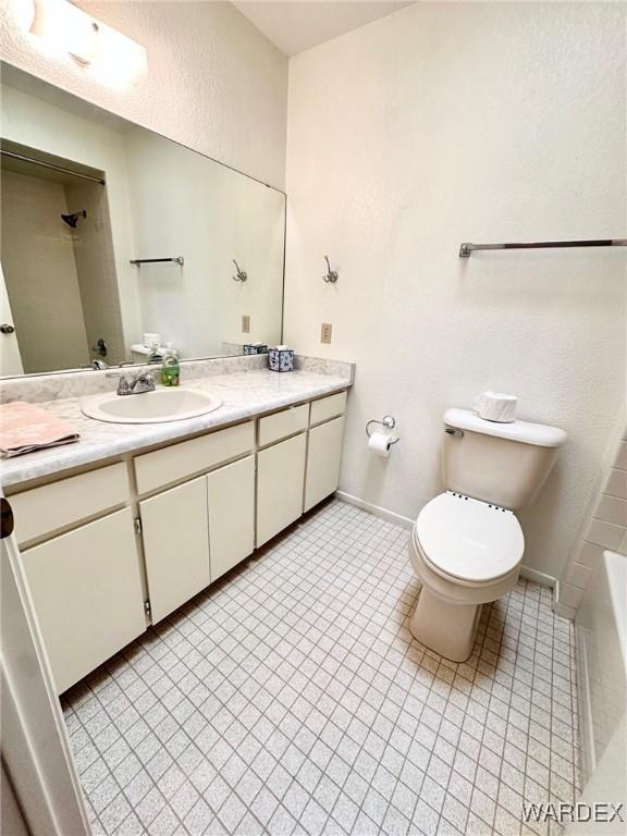 full bathroom with a bathing tub, vanity, toilet, and baseboards