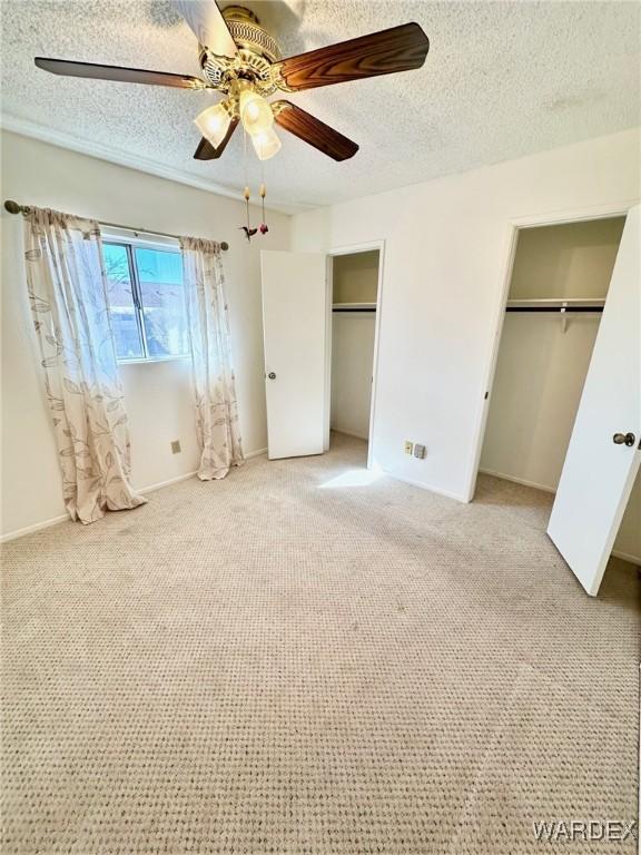 unfurnished bedroom featuring multiple closets, light carpet, ceiling fan, and a textured ceiling