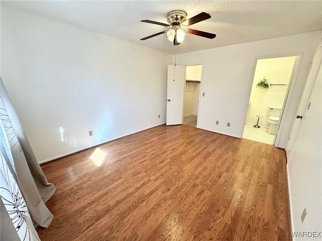 unfurnished bedroom featuring light wood-type flooring, a textured ceiling, ensuite bath, and a spacious closet