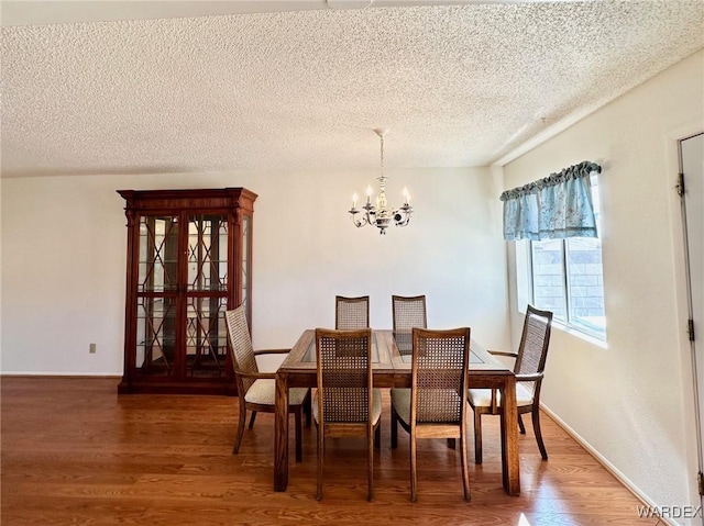 dining space with an inviting chandelier, a textured ceiling, baseboards, and wood finished floors