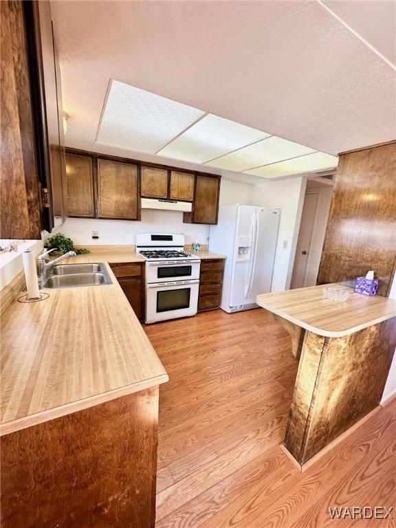 kitchen with white appliances, under cabinet range hood, light countertops, light wood-style floors, and a sink